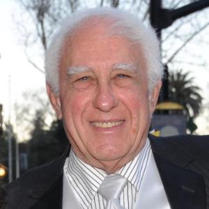 A person smiling with a background of trees and lampposts.