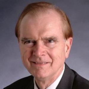 A man in a suit and red tie against a dark background.