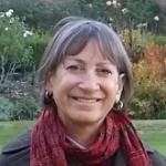 A woman in a garden wearing a red scarf and a grey coat.