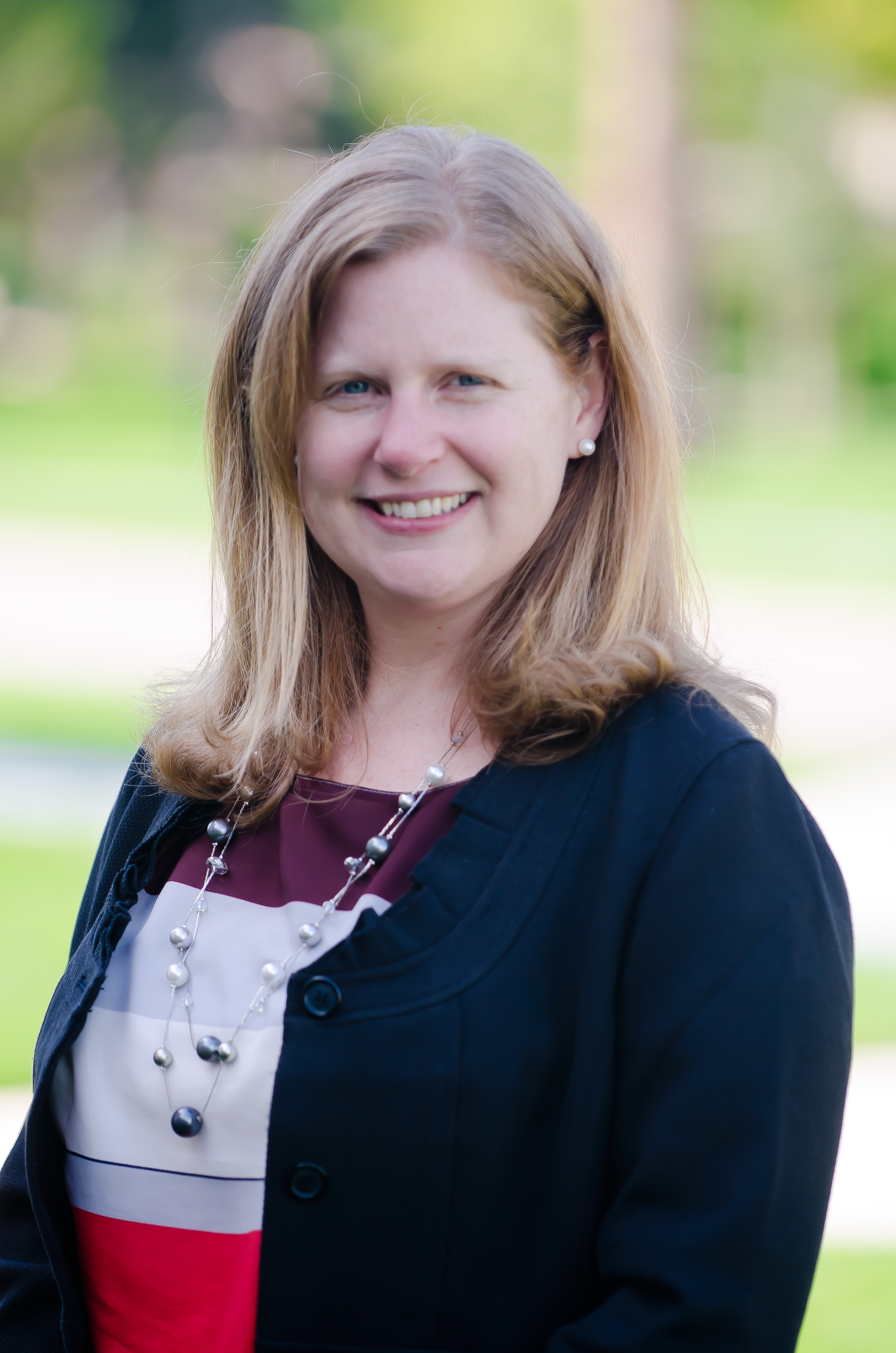 photo of becky konowicz dean of admission she is a white woman with strawberry blond hair she is wearing a long necklace with pearls, a silk shirt that is pink, white and maroon striped, and a blue back with collar ruffles