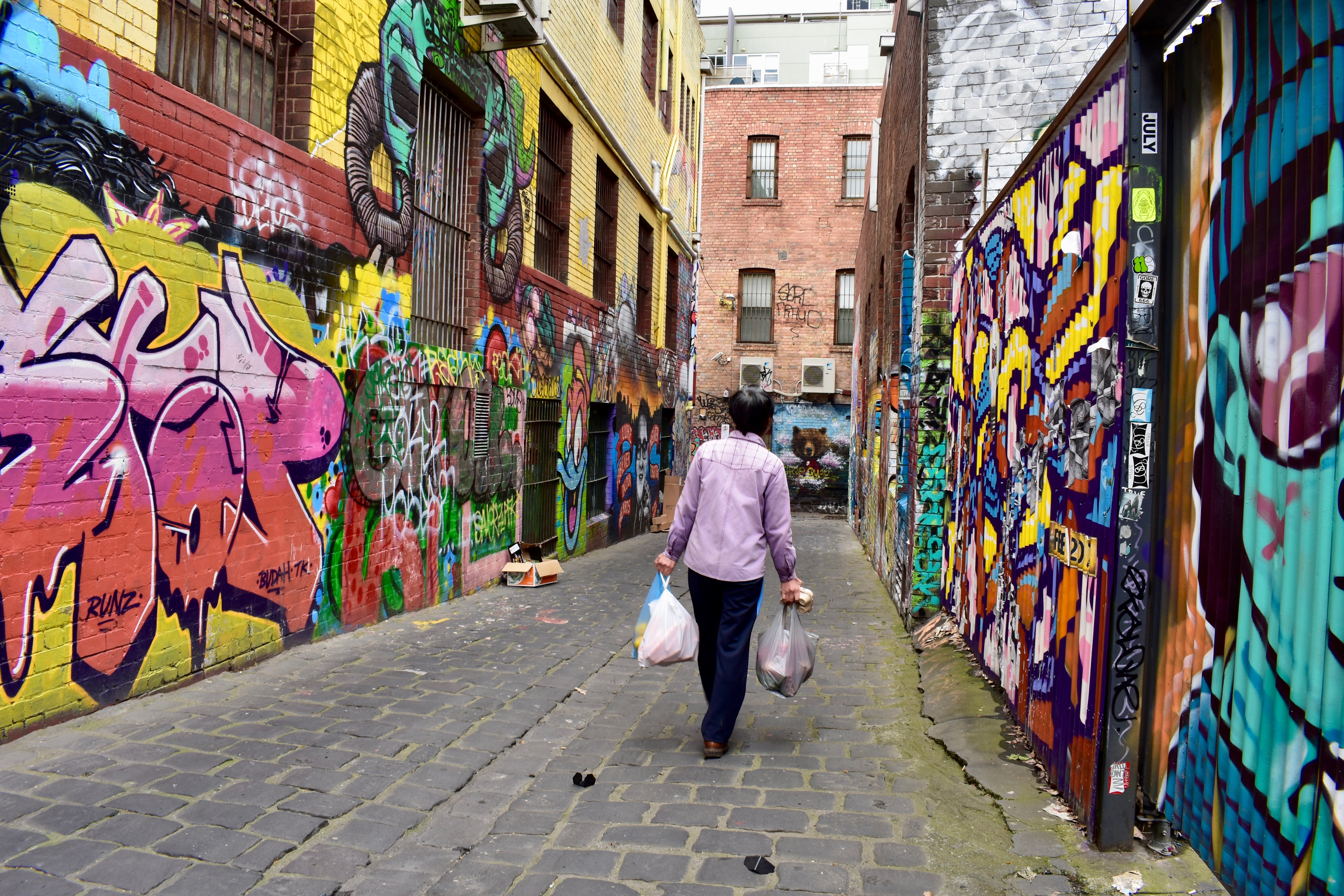Person walking in graffiti-covered alley with grocery bags.