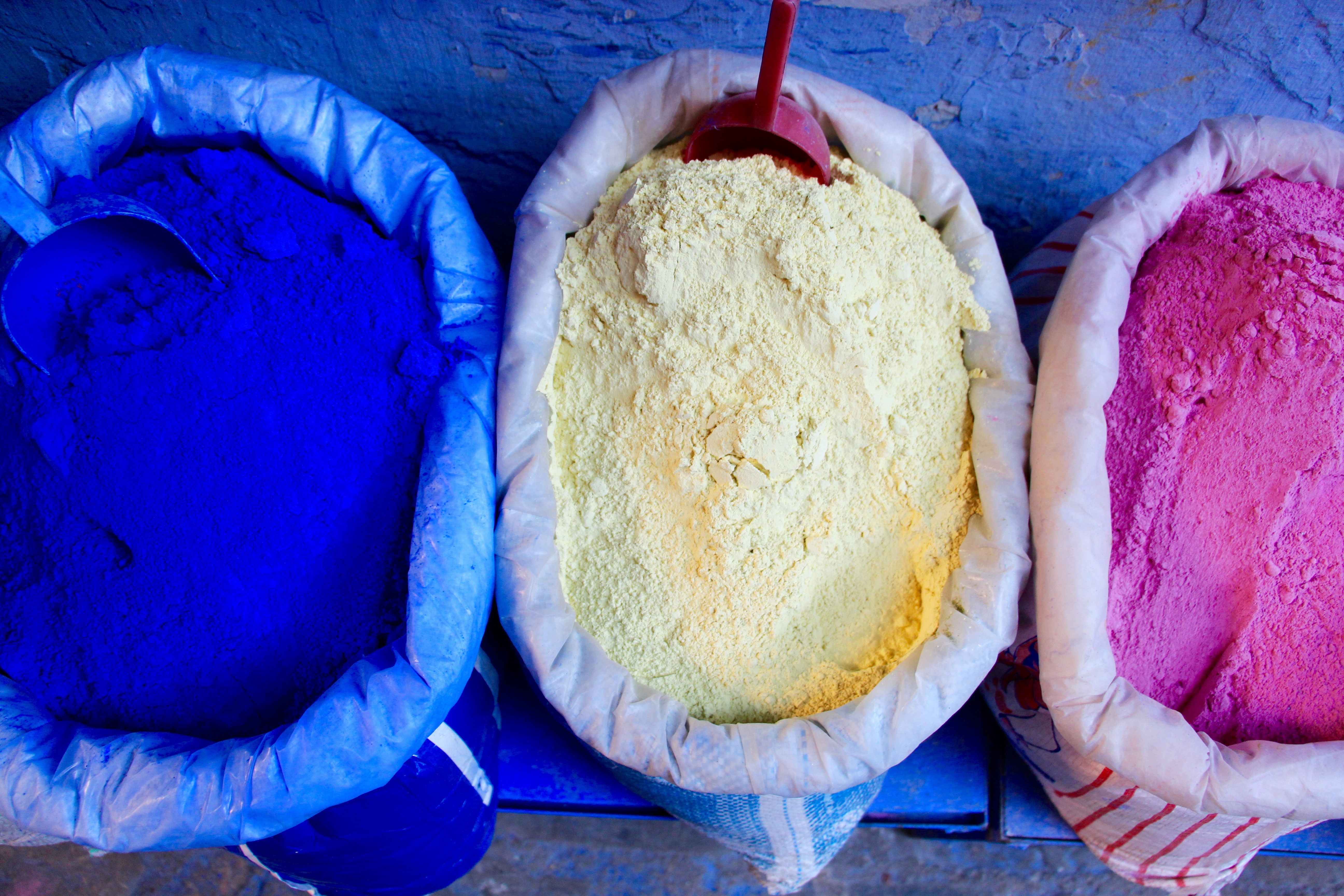 Three containers with blue, yellow, and pink powdery substances.