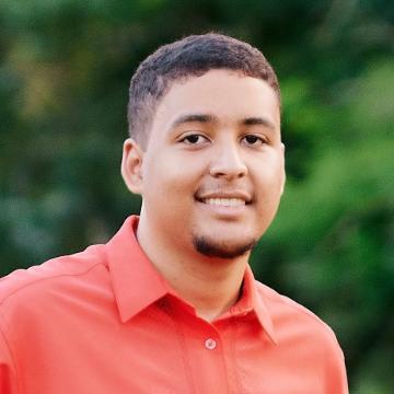 A person in a red shirt smiling with a green background.