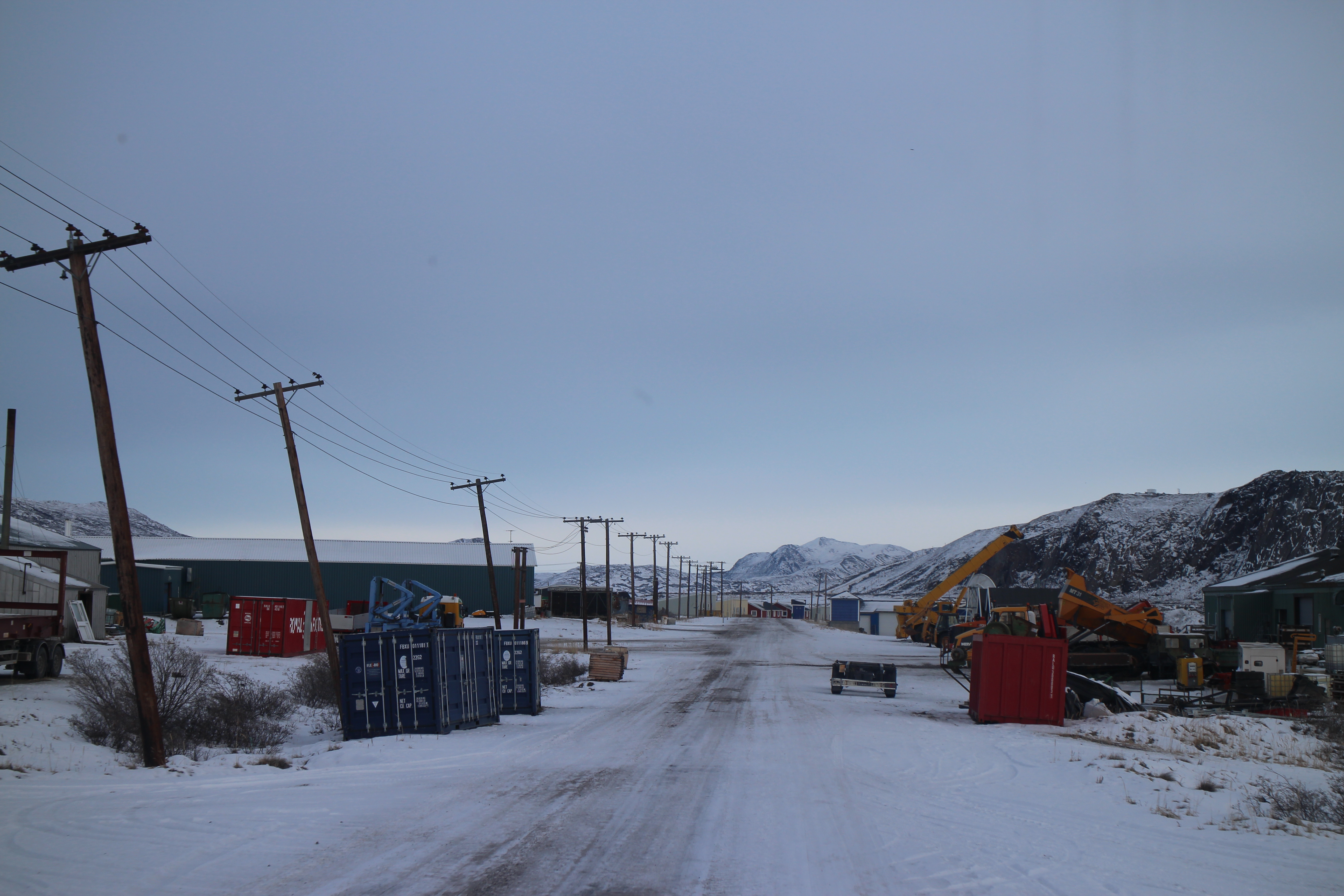 Snow-covered road with power lines and vehicles on both sides.
