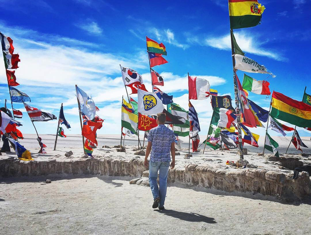 Person standing among numerous flags against a bright blue sky.