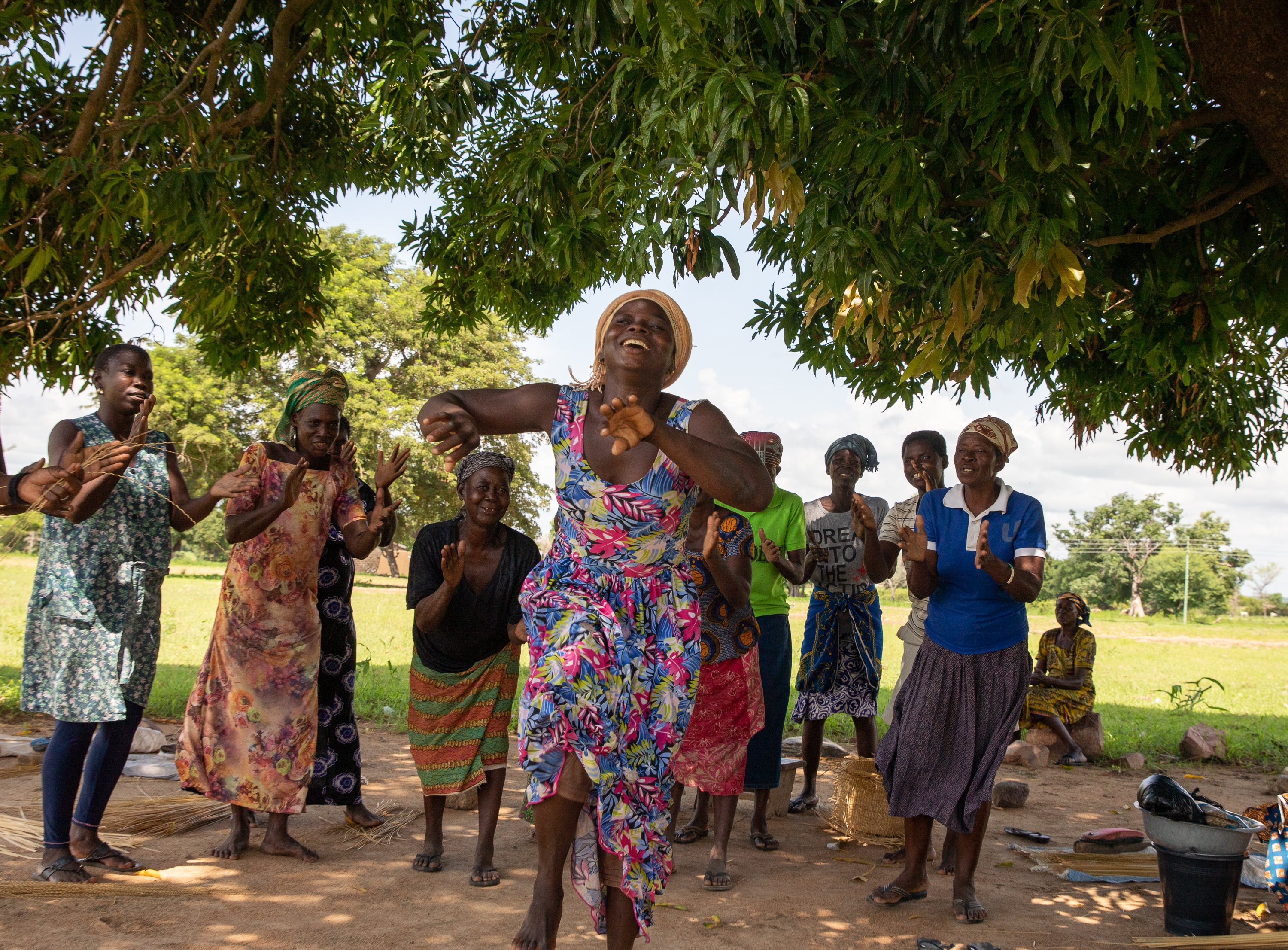A group of people interacting outdoors under a tree's shade in Ghana.