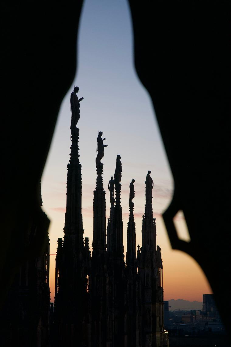 Duomo di Milano in Milan, Italy; statues of people in dark silhouette with sunset background -  Duomo di Milano in Milan, Italy; statues of people in dark silhouette with suns Link to file