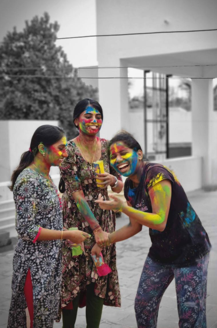 Three girls celebrating Holi, covered in colors, with black and white background