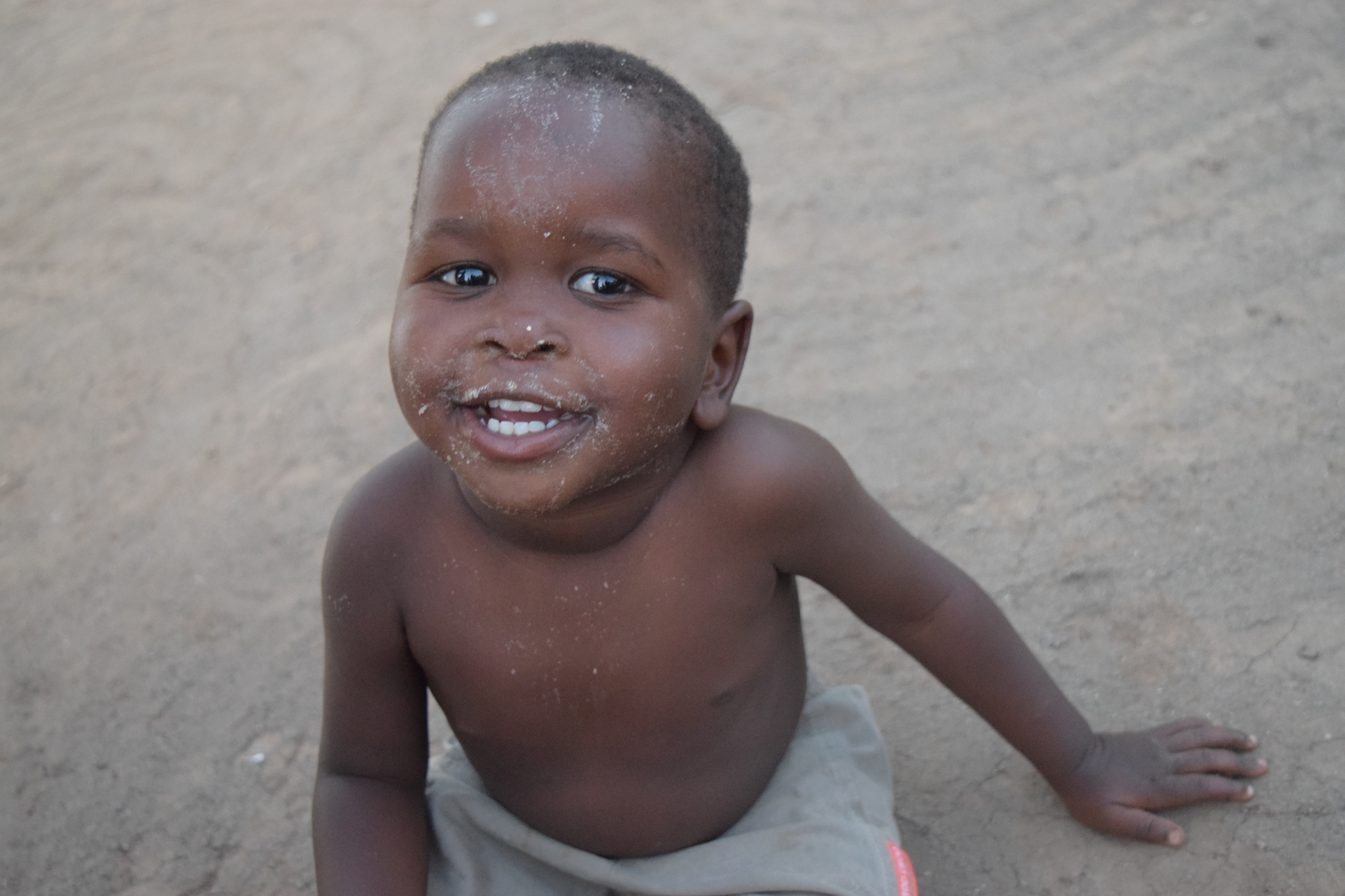 A smiling child sits on the ground.