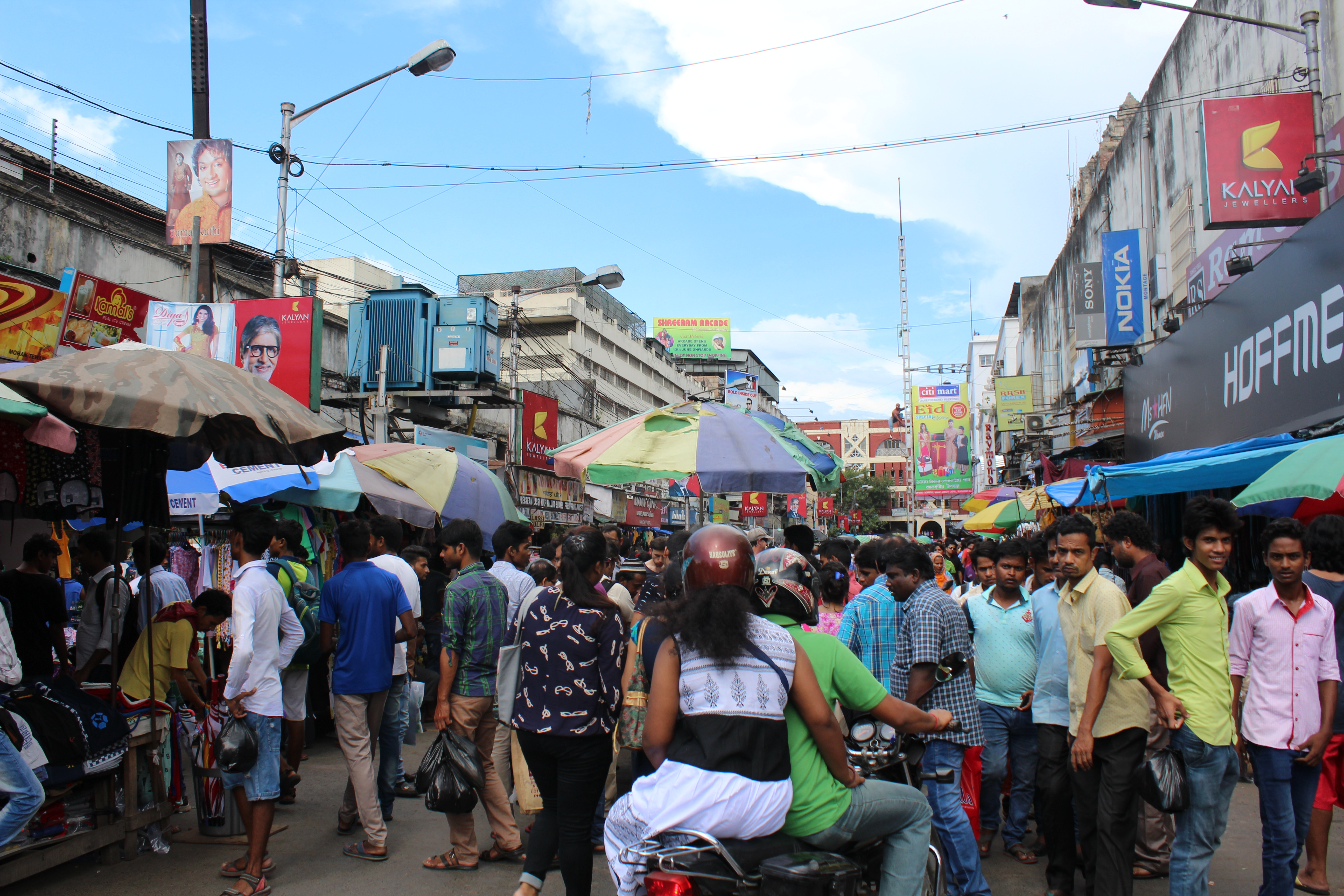 A crowded street market with people and stalls under a clear sky.