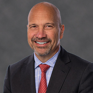Headshot of man with a mustache smiling in jacket and tie.