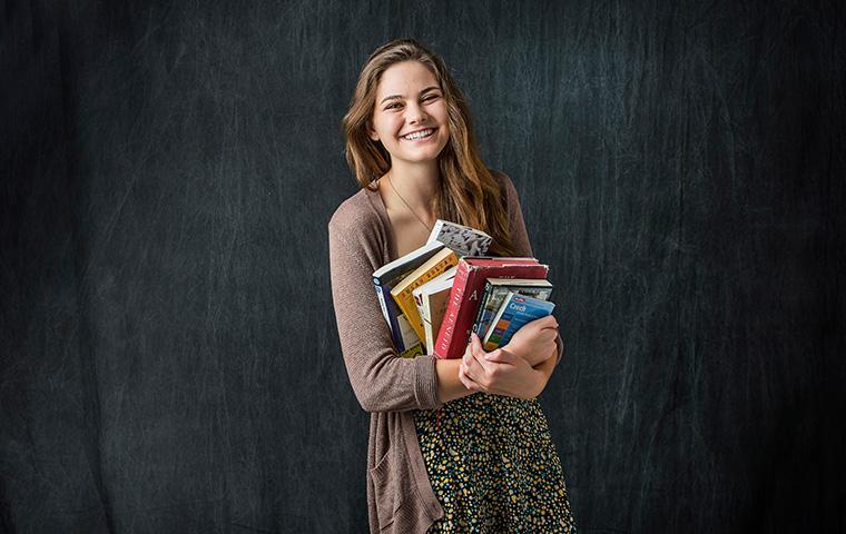 A person smiling and holding books against a dark background.