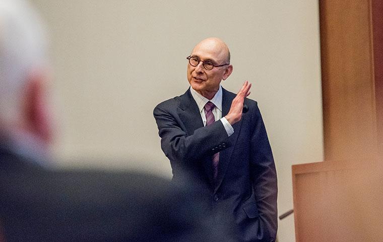 A man in a suit lecturing to an audience.