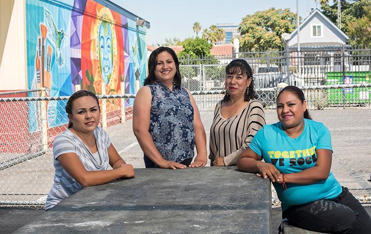 Four women smiling and sitting at a picnic table outdoors.