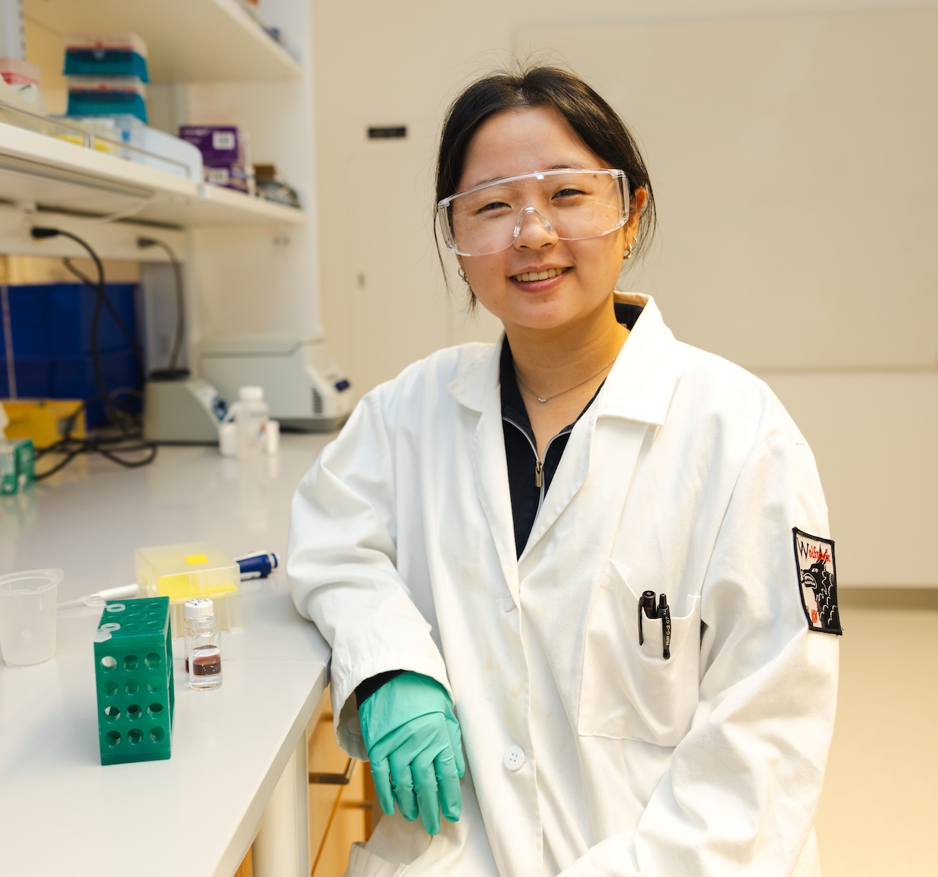 Rebecca An, wearing a lab coat in a chemistry laboratory.