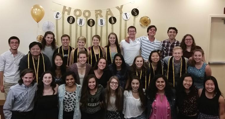Group of students smiling for a graduation party under a banner that says congrats. 