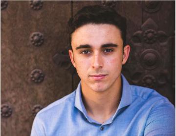 A person in a blue shirt sitting in front of a wooden background.