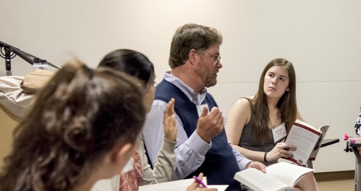 People in a discussion, one speaks while others listen and take notes.