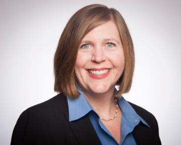 A person smiling, wearing a black blazer and blue shirt.