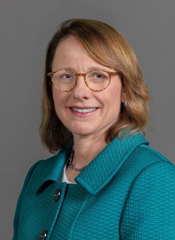 Photo of Dr. Kendra Sharp, a female with light brown hair and glasses, wearing a teal suit jacket.