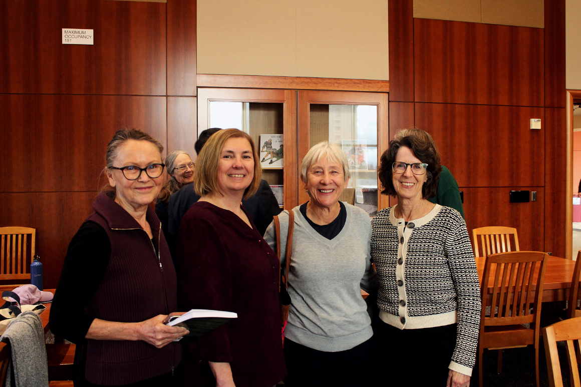 four women stand and smile together