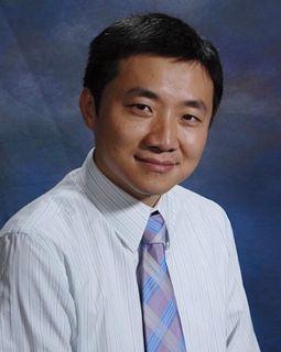 A person smiling, wearing a white shirt and tie against a blue background.