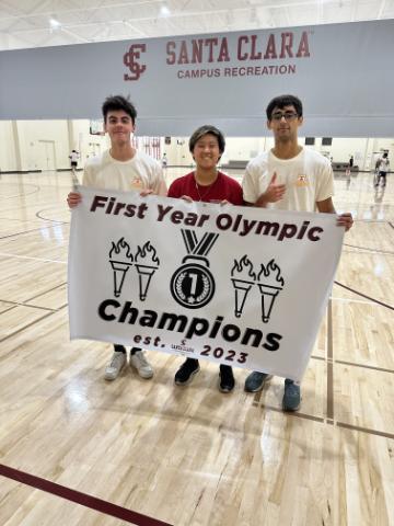 Three students from team alpha hold up the first year olympics sign.