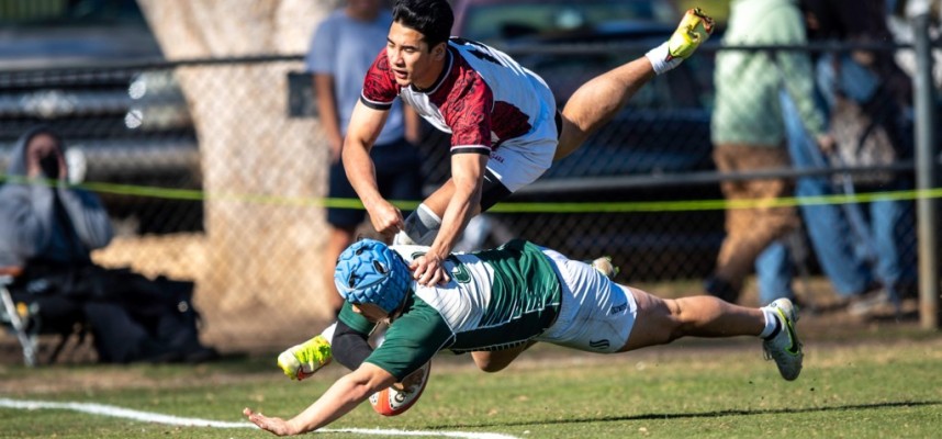 Rugby players mid-tackle, one in green uniform being brought down by another.