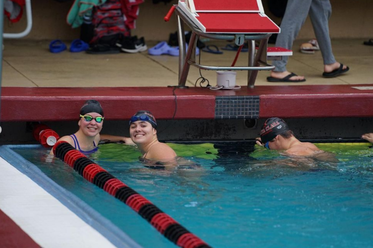 Picture shows three swimmers in the water, two of which are smiling at the camera.
