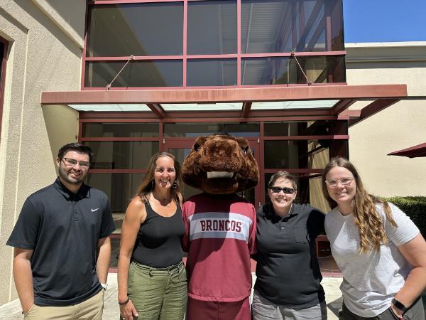 4 Full time staff smile with bucky, the school mascot, in front of the facility. From left to right is Austin Hunt, Janice DeMonsi, Katheryn Huthings, and Kelly Frumkin