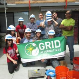People in hard hats smile while holding a banner that says grid alternatives. Links to Renewable Energy Certificate page.