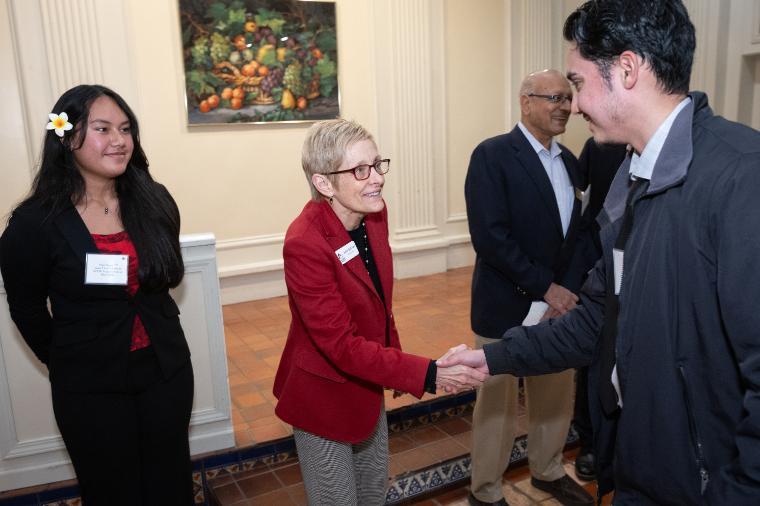 A student shaking hands with Julie Sullivan while another student looks on.