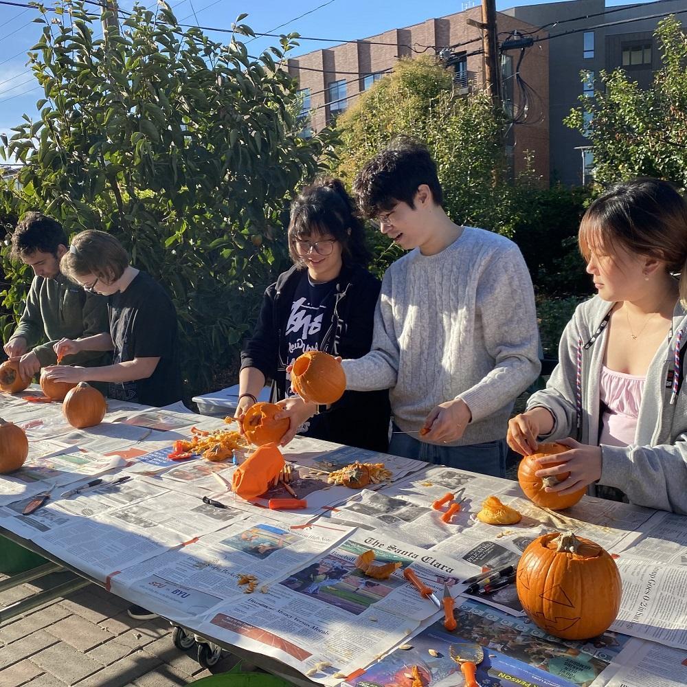 A group of students carve small pumpkins on a table.