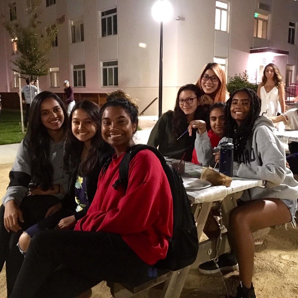 A group of students sit on tables in front of the residence halls