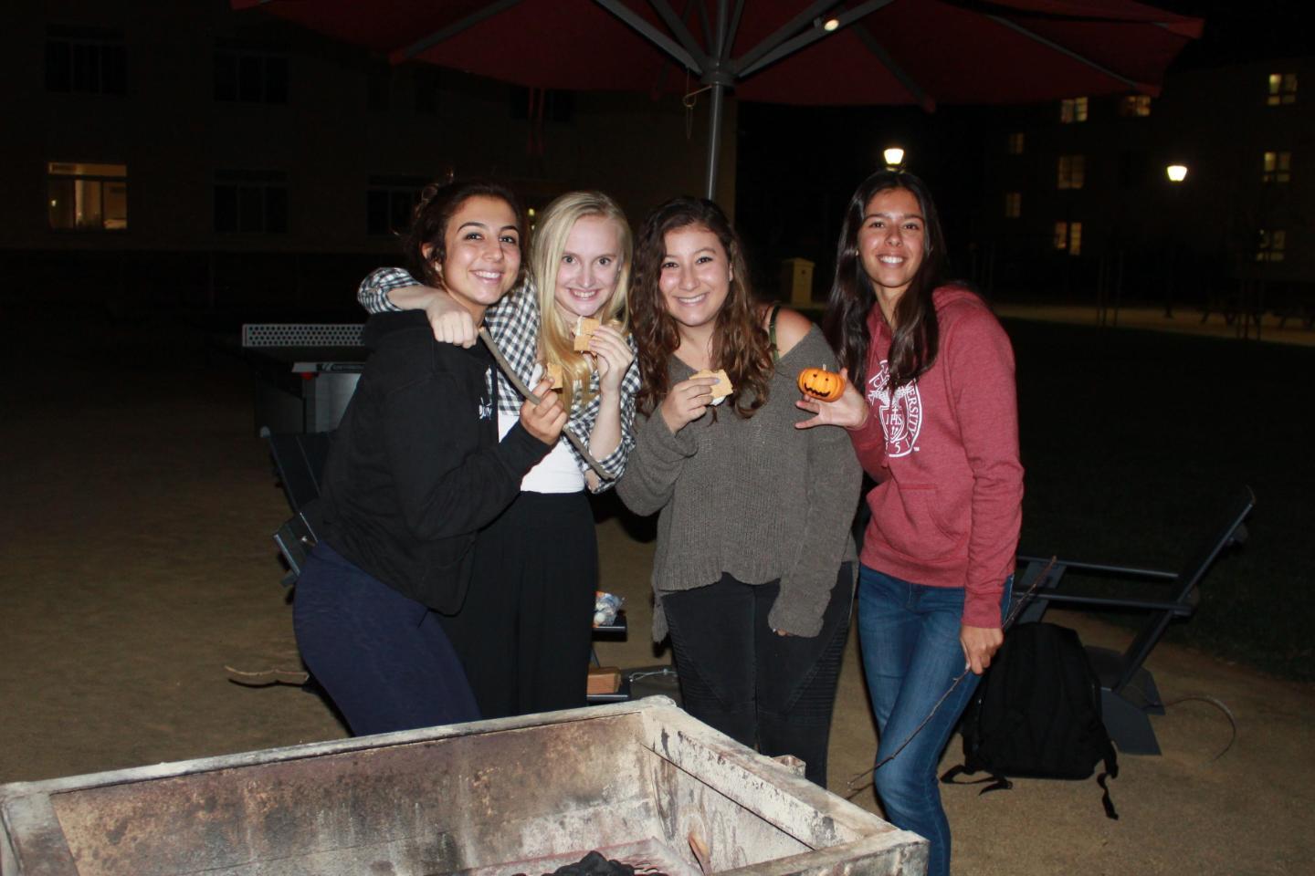 Four students smile holding smores outside at night