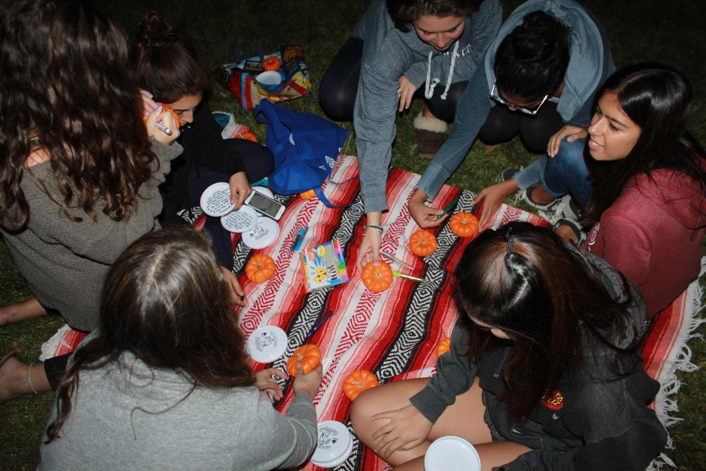 Overhead view of students sitting on a blanket and decorating pumpkins outside at night