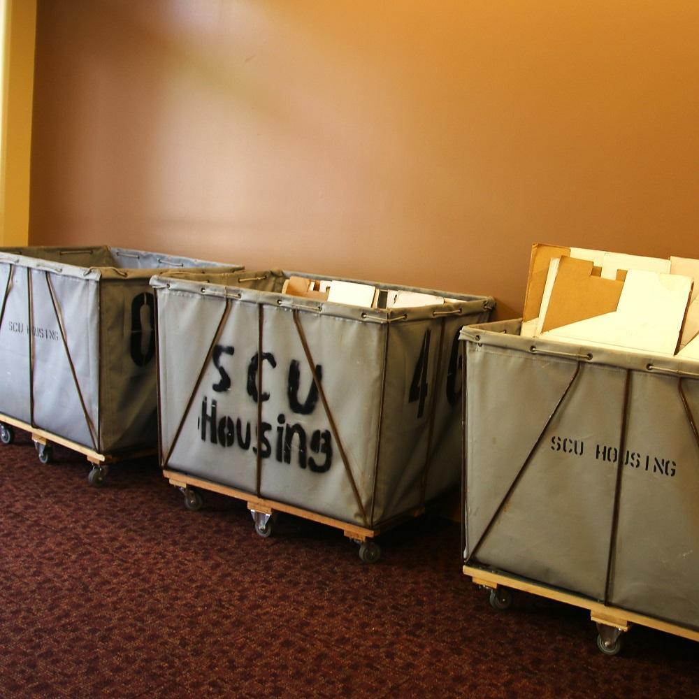 Three canvas bins on wheels in a row against a wall