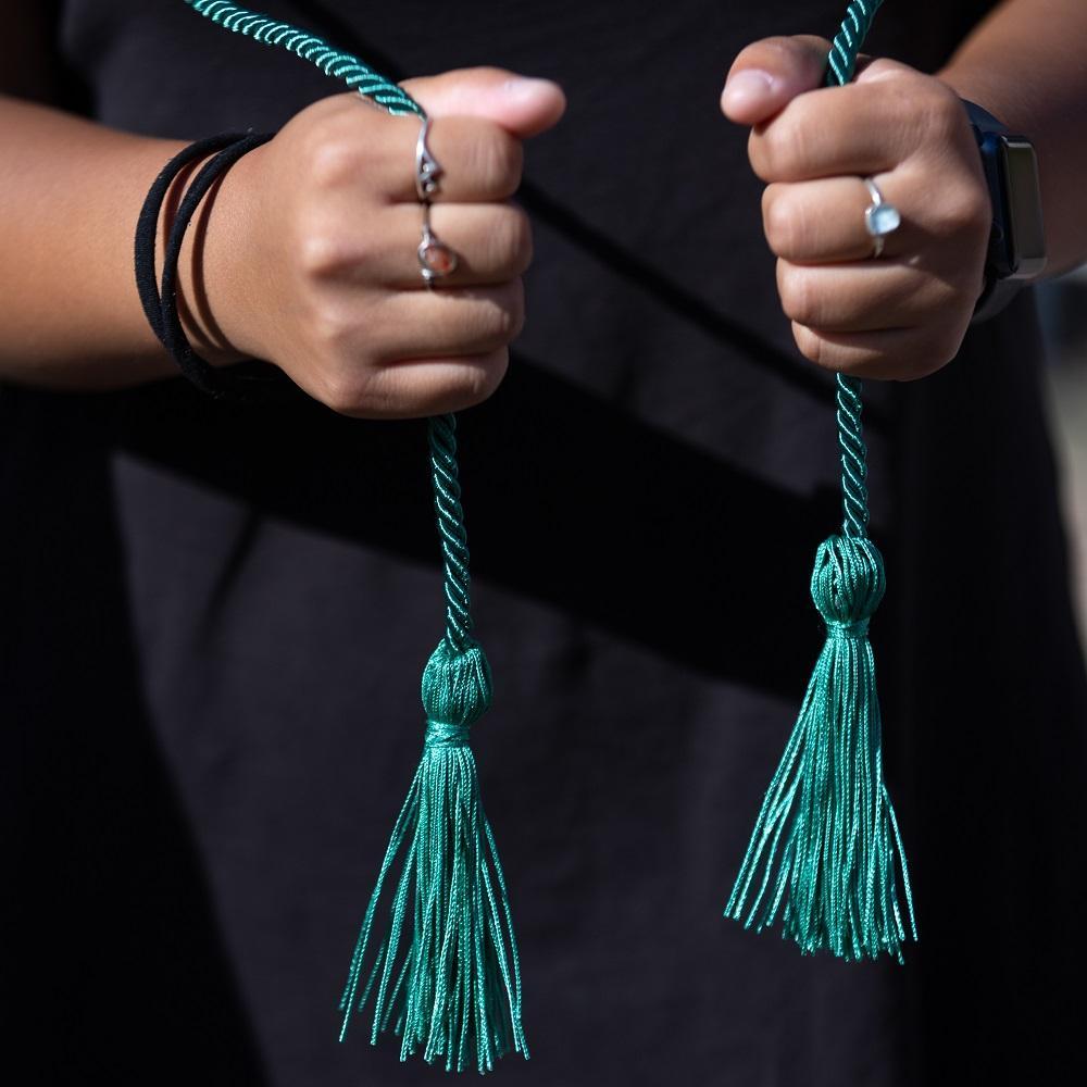 A student holding a green sustainability graduation cord in front of them
