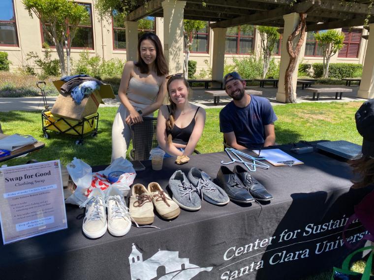 Three students smile behind a Center for Sustainability table with shoes and a scale on it