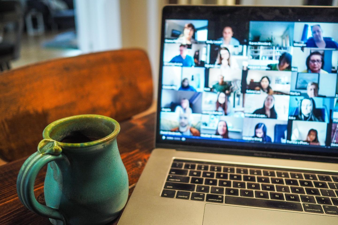 A laptop displaying a virtual meeting next to a coffee cup on a table, Photo by Chris Montgomery on Unsplash
