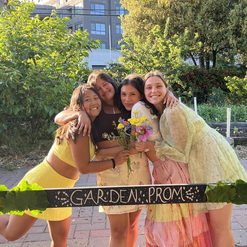 Four students in yellow dresses pose behind a frame decorated with flowers