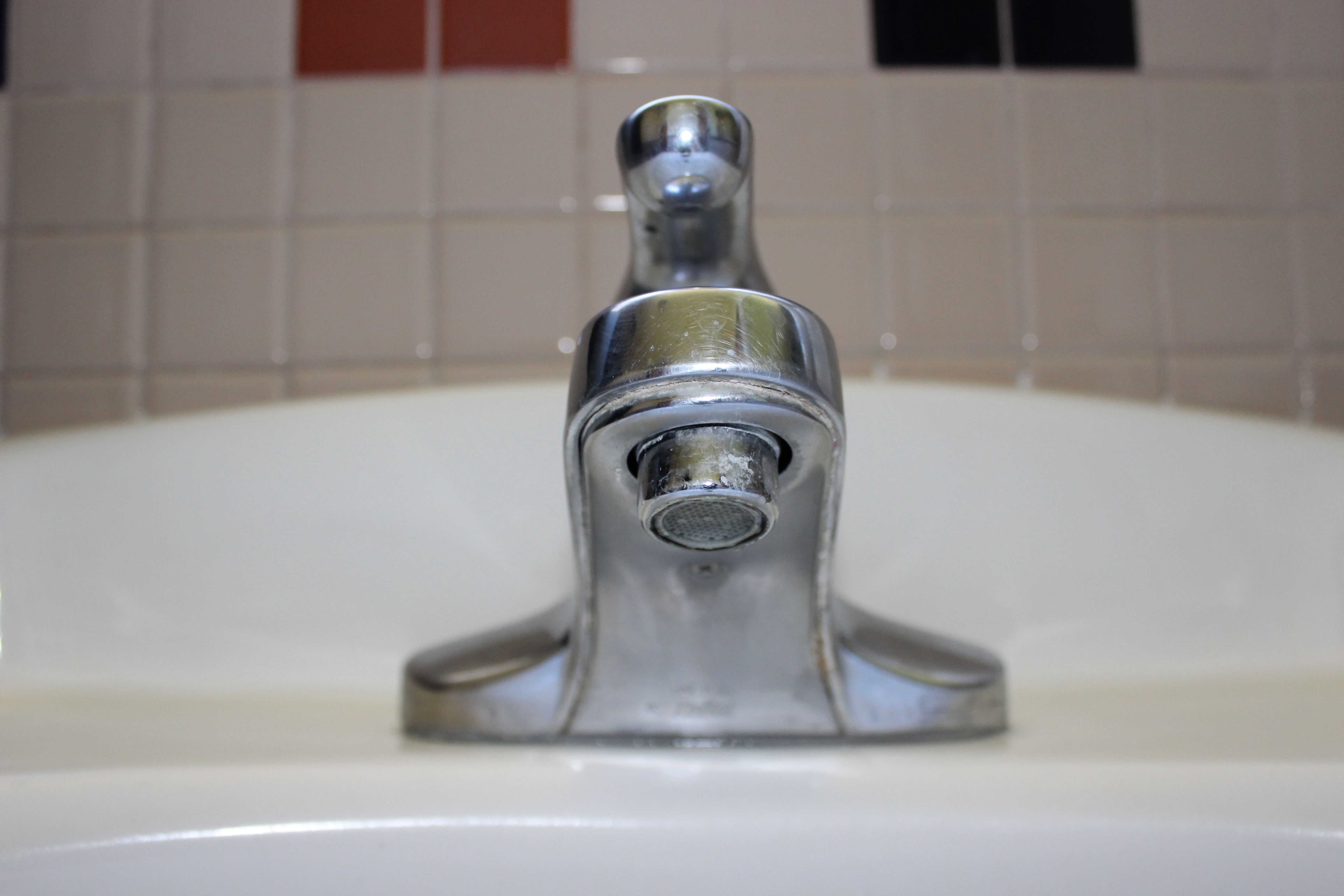A silver bathroom sink faucet with tiled backsplash.