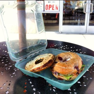 Open eco-friendly container with a bagel sandwich inside on a table.