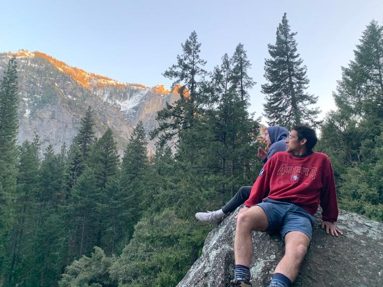 Eemon Ghasemiyeh sitting outside overlooking a mountain and tall forest trees