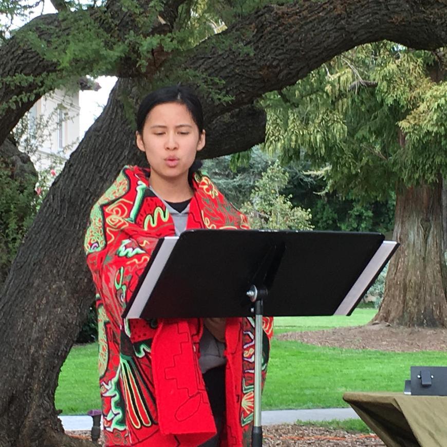 Alumna wrapped in red blanket reads Laudato Si under a tree