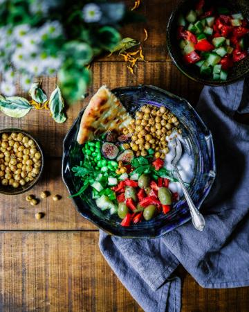 A plant based bowl with chickpeas pita olives peppers and other veggies sitting on a table