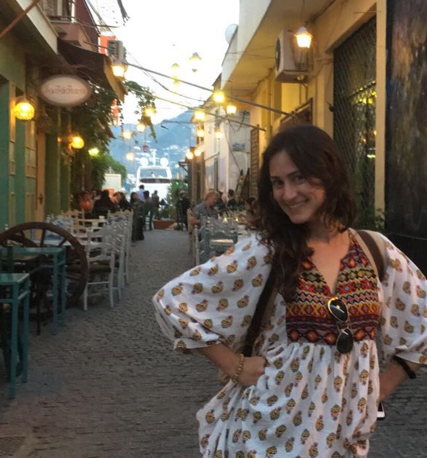 A person posing in a lit, narrow street lined with shops and string lights.