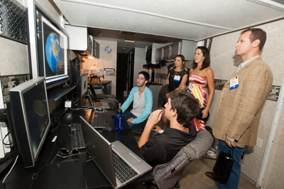 Group of people working with monitors and electronics in a room.