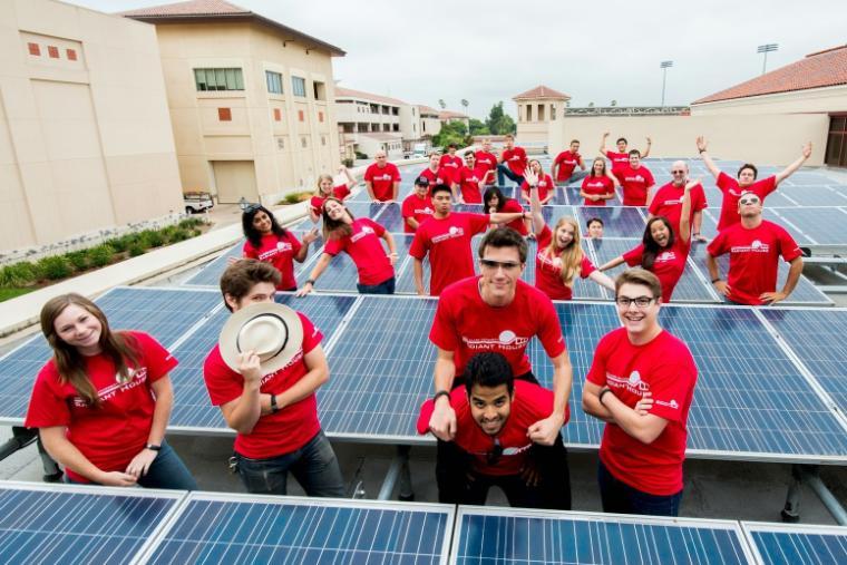 Group of people wearing red shirts, posing playfully on solar panels. image link to story