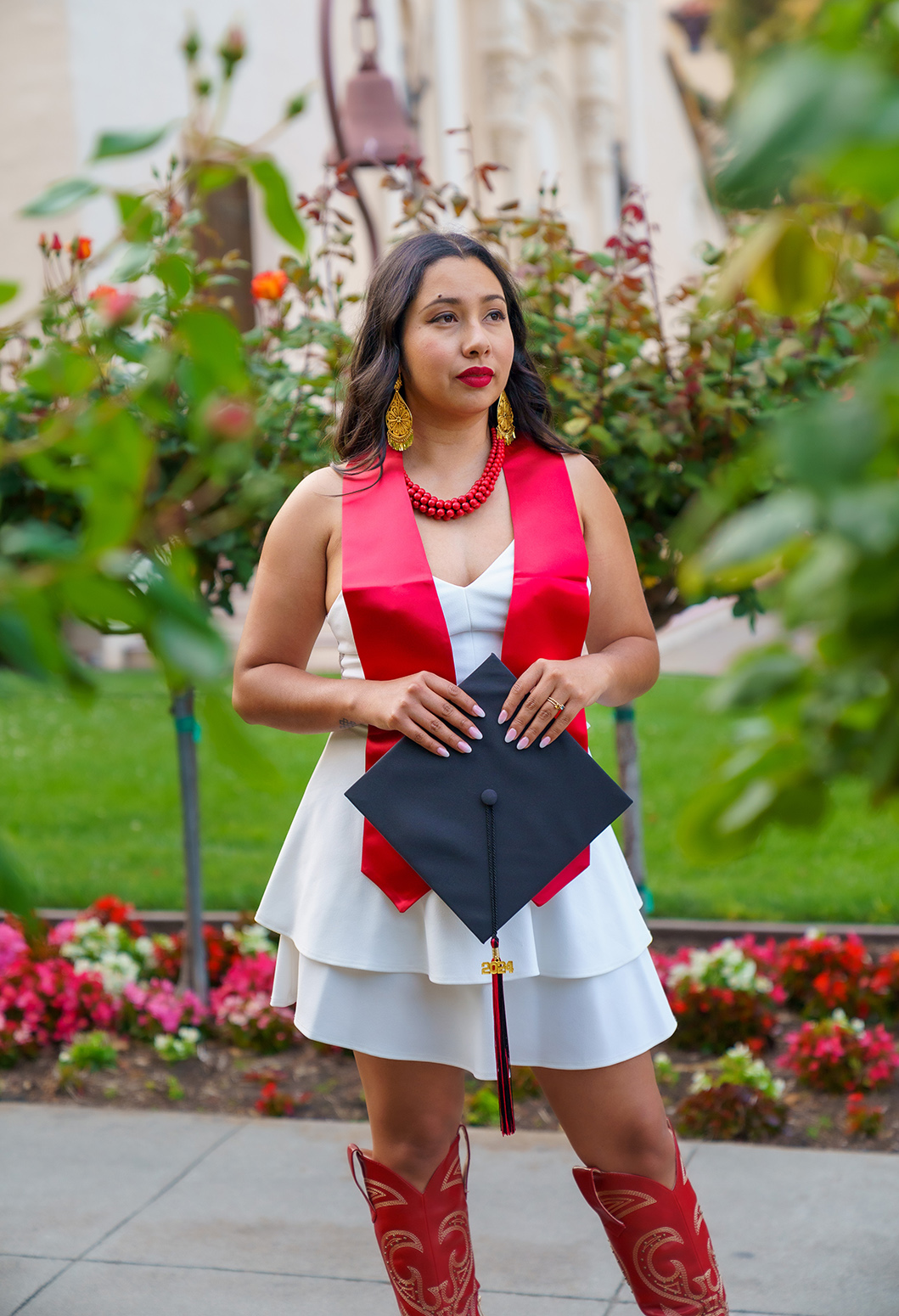 A female student in a white dress holding her graduation cap.
